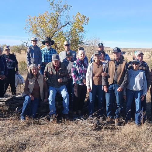 A group of about 20 people pose on a dry prairie site