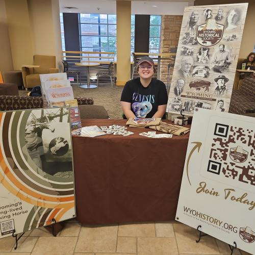 Person sits at a table surrounded by posters with information about the Wyoming Historical Society