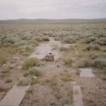 The powerhouse foundation and part of the concrete directional arrow from the field at Dana, Wyo., show through the sagebrush, 2009. Author photo.