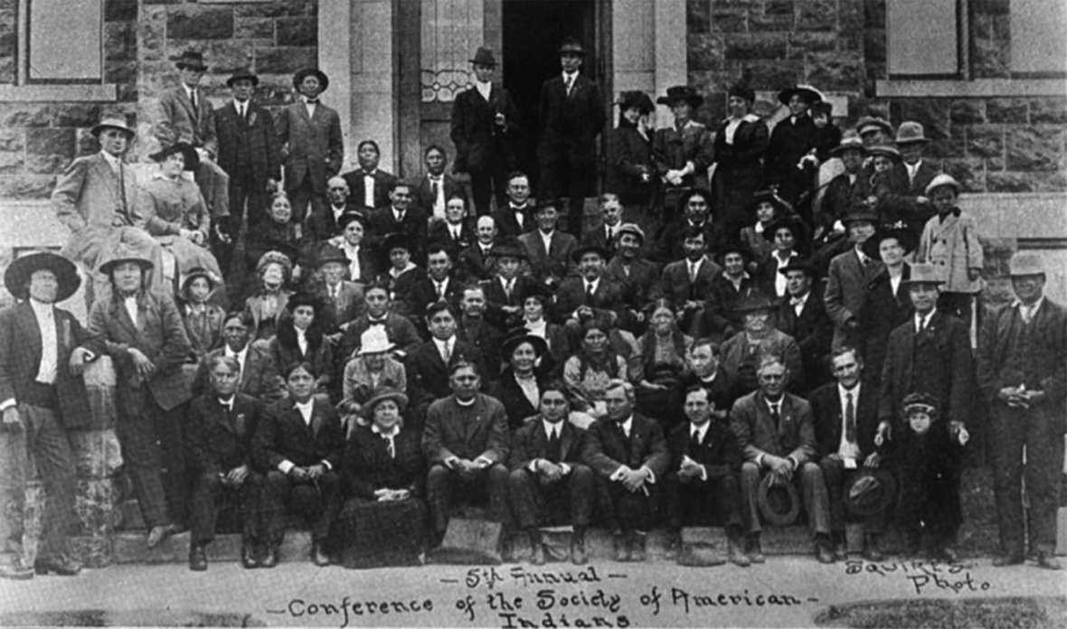 Attendees at the fifth annual conference of the Society of American Indians, 1915. Sherman Coolidge, in clerical collar, is near the center of the front row.  His time in the Society softened his views on assimilation considerably, and he began to view Indian cultures as valuable. Wikipedia. 