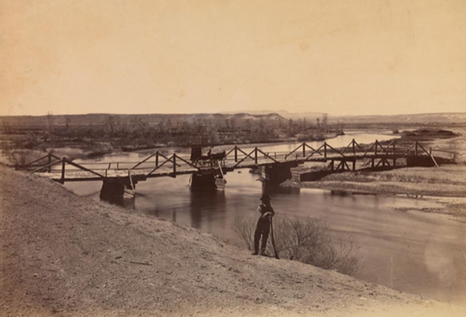 Bridge across the Laramie River near its junction with North Platte River, 1868. The standing man may be Alexander Gardner. William T. Sherman collection of Alexander Gardner photographs; National Museum of the American Indian (NMAI) Archive Center, Smithsonian Institution.