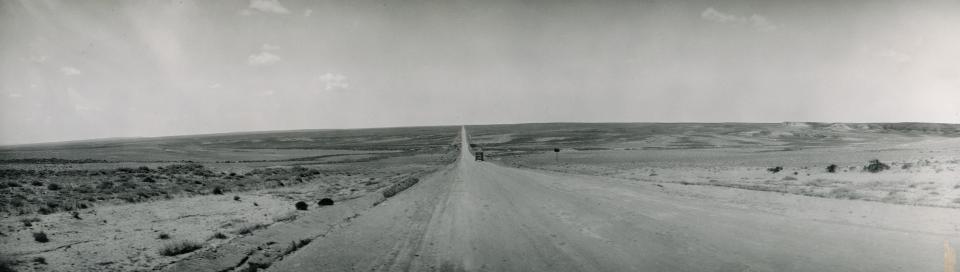 Black and white photo of wide plain without trees looking down road heading toward the horizon