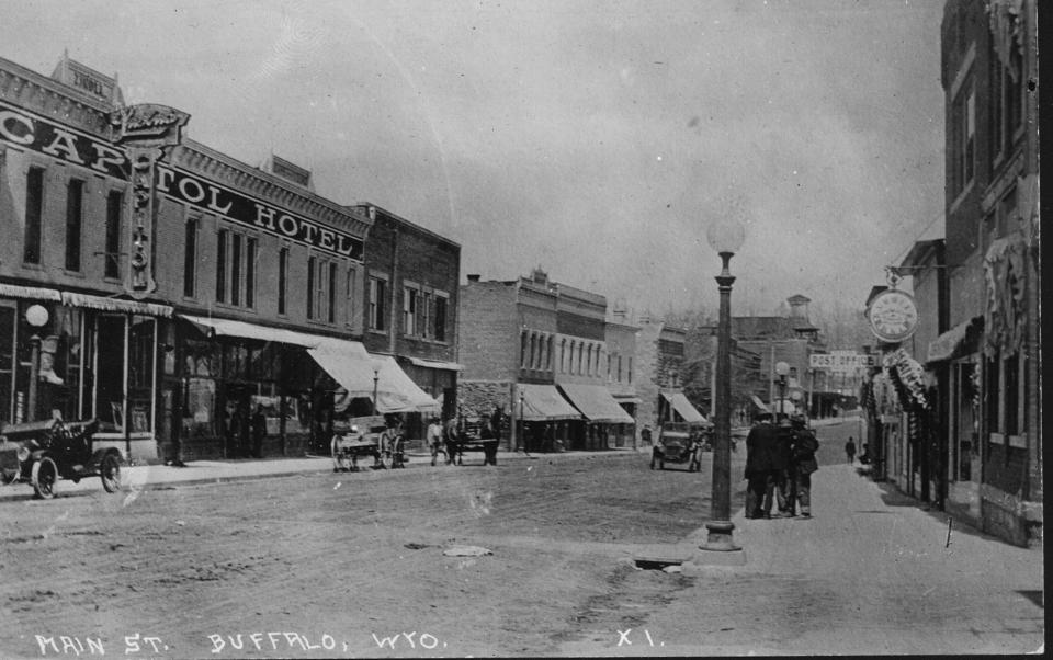 The Capitol Hotel fronts dirt Main Street of Buffalo, Wyoming, with some early automobiles present, as well as horse-drawn wagons.