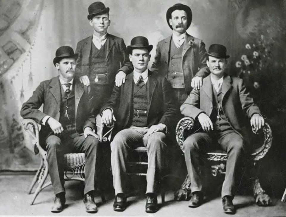 Five men in suits an bowler hat pose for a portrait in a photography studio