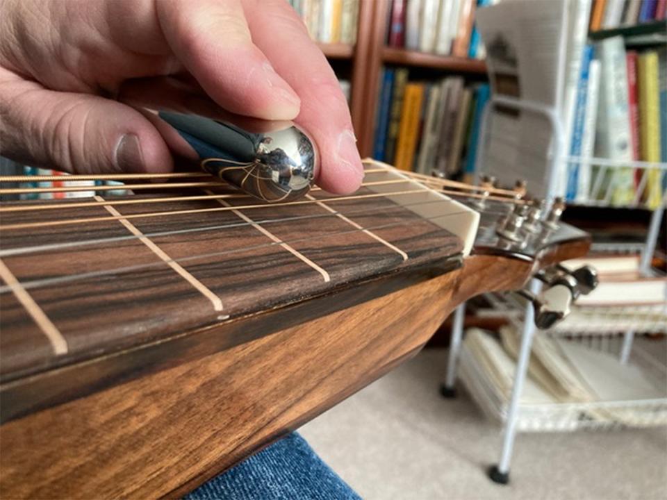 On the neck of a steel guitar, the strings are raised by a nut well above the frets and the player, with his left hand, moves a steel or tone bar along the strings to define the notes. Strings are then plucked by the right hand to create the sounds. Movements of the bar create the wavering tones associated with the instrument. Author photo.