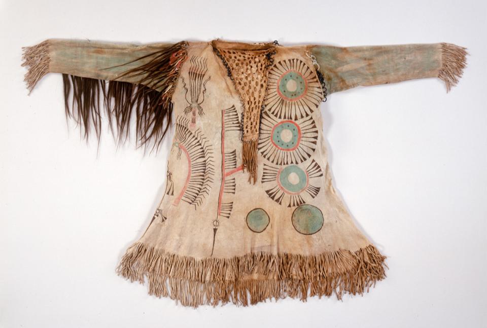 Exceptional Upper Missouri Region man’s shirt, about 1858. The painted abstract designs represent shields, lances, fans and war bonnets. Other decorations of the fringed garment include hair, feathers and glass beads.  National Museum of the American Indian (hereafter NMAI), Smithsonian Institution, catalog number  8/8017.