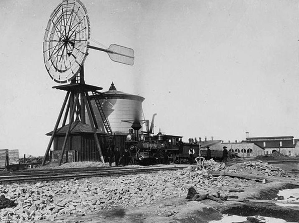 A windmill at Laramie drew water for steam locomotives, ca. 1869. Roundhouse and machine shops at back right. A. J. Russell, Wikipedia. 