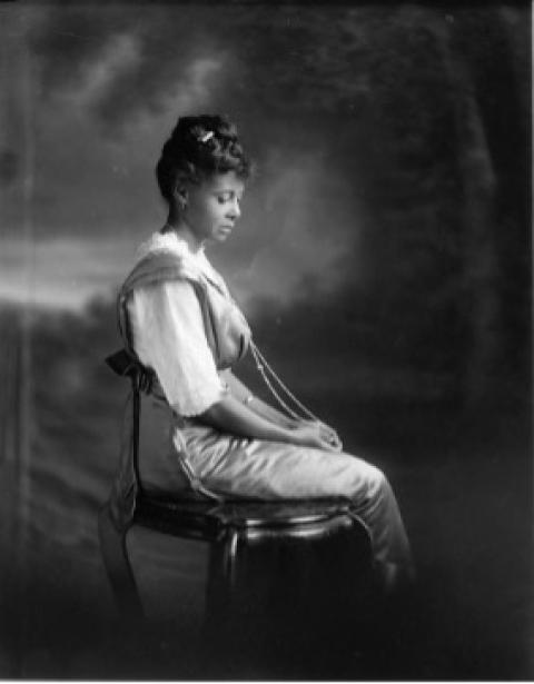 A young Balck woman poses ina chari with downcast eyes