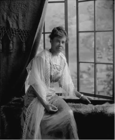 Black oman ina long dress with a lace shawl poses in front of an open window