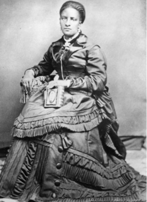 Black woman in an elaborately ruffled dress poses while seated.